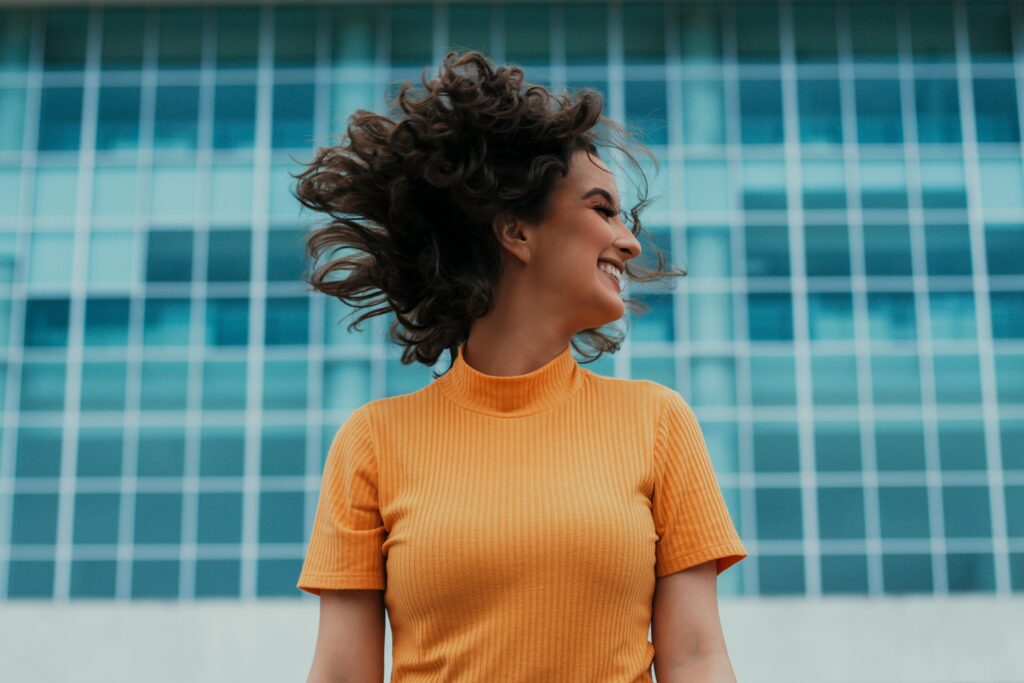 Cheerful woman smiling and flipping her hair in front of a modern building.